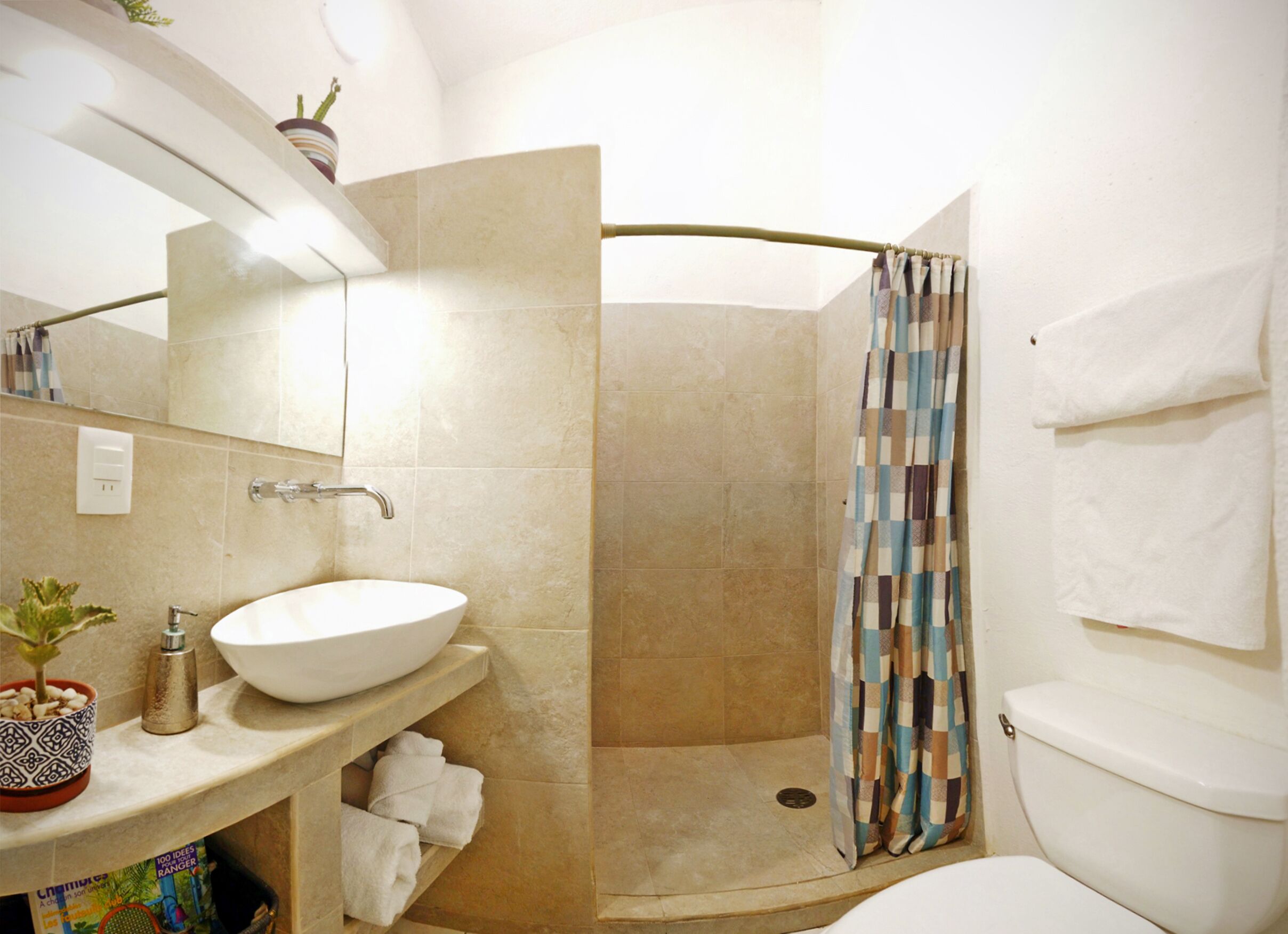 A bathroom with a white sink, a shower with a checkered curtain, a toilet, and a mirror above the sink.
