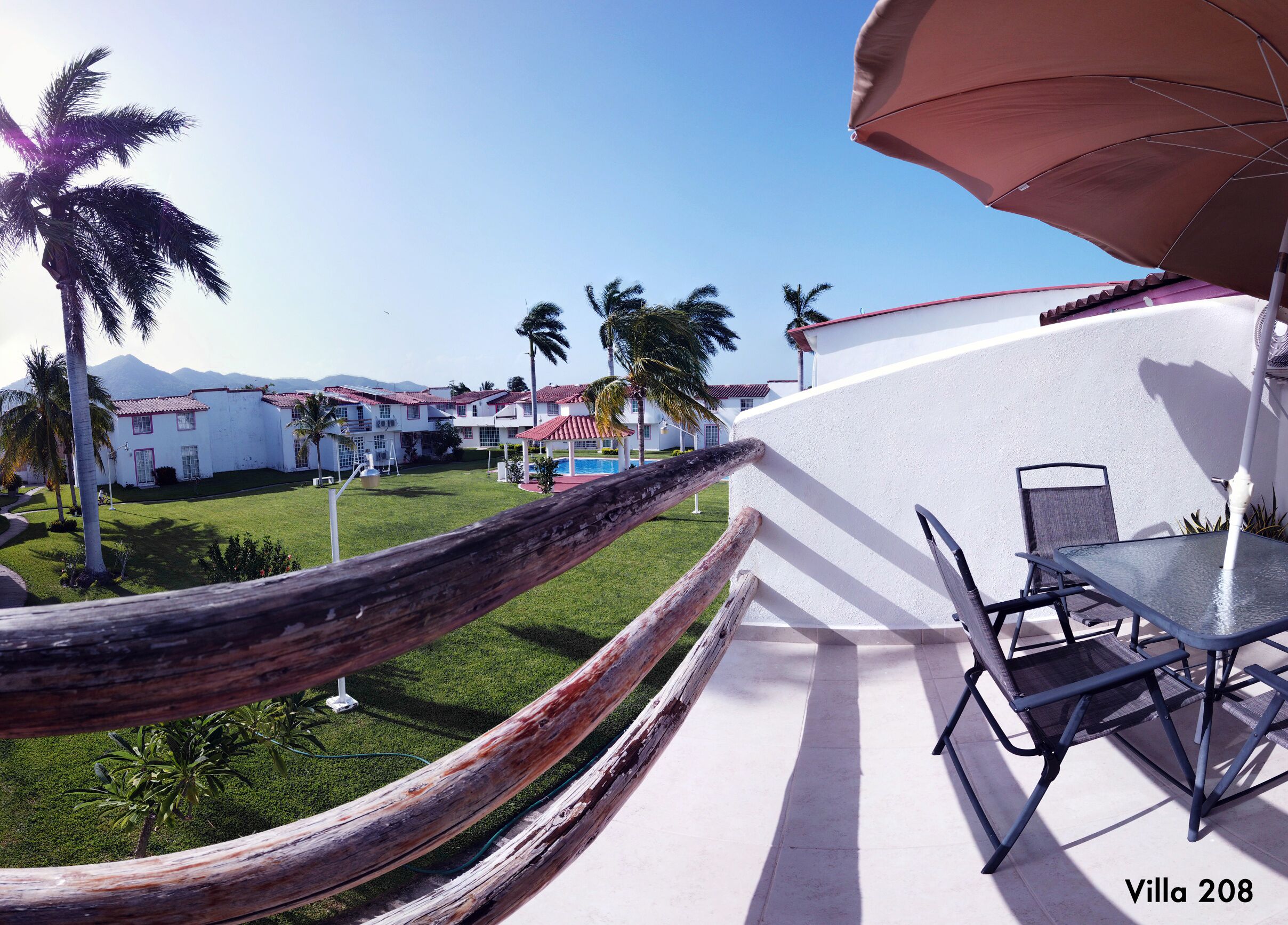 A hammock on a balcony overlooking a pool and a view of villas.