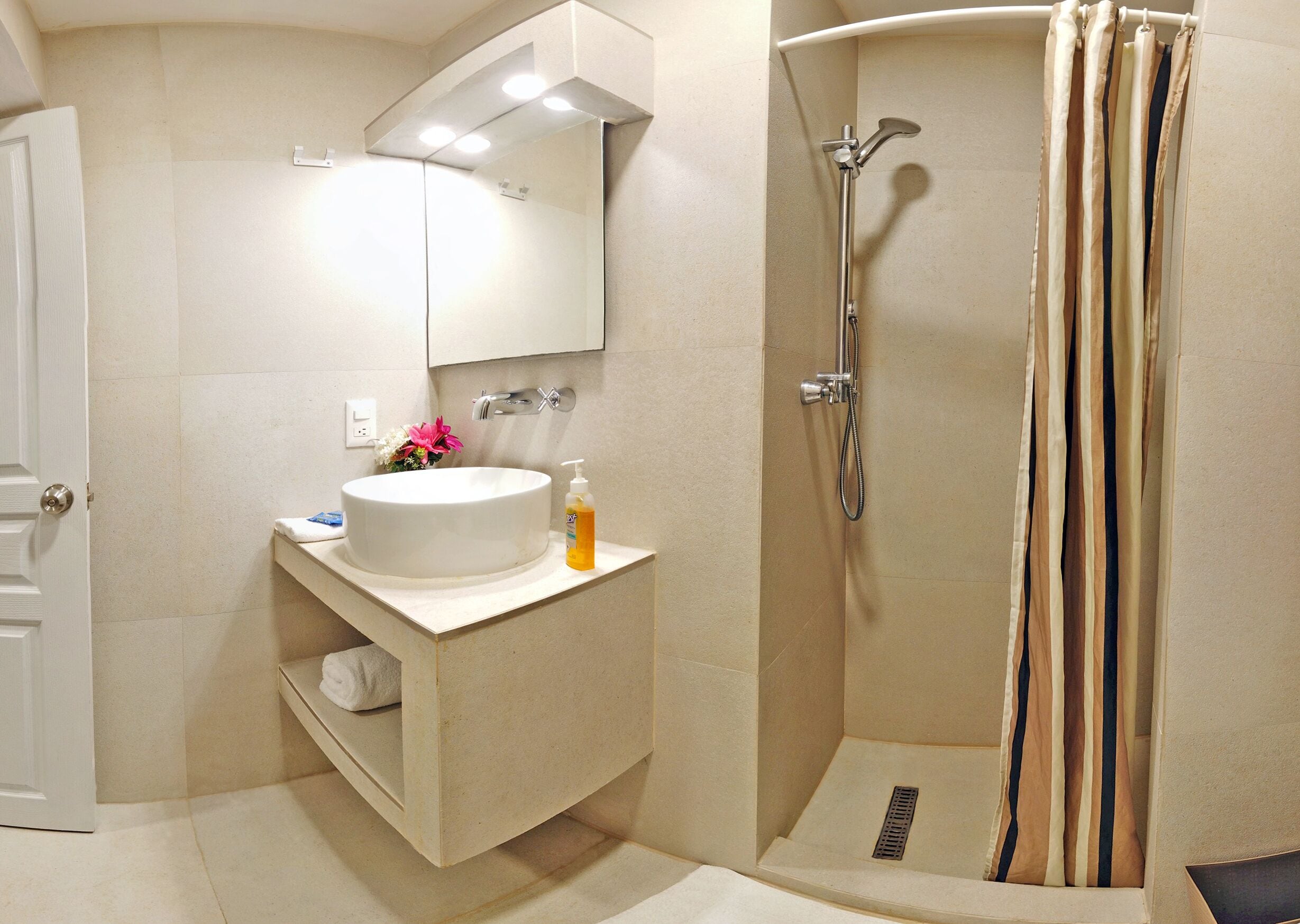 Un baño con un lavabo blanco, un espejo, una ducha con cortina a rayas y un estante pequeño con una toalla.