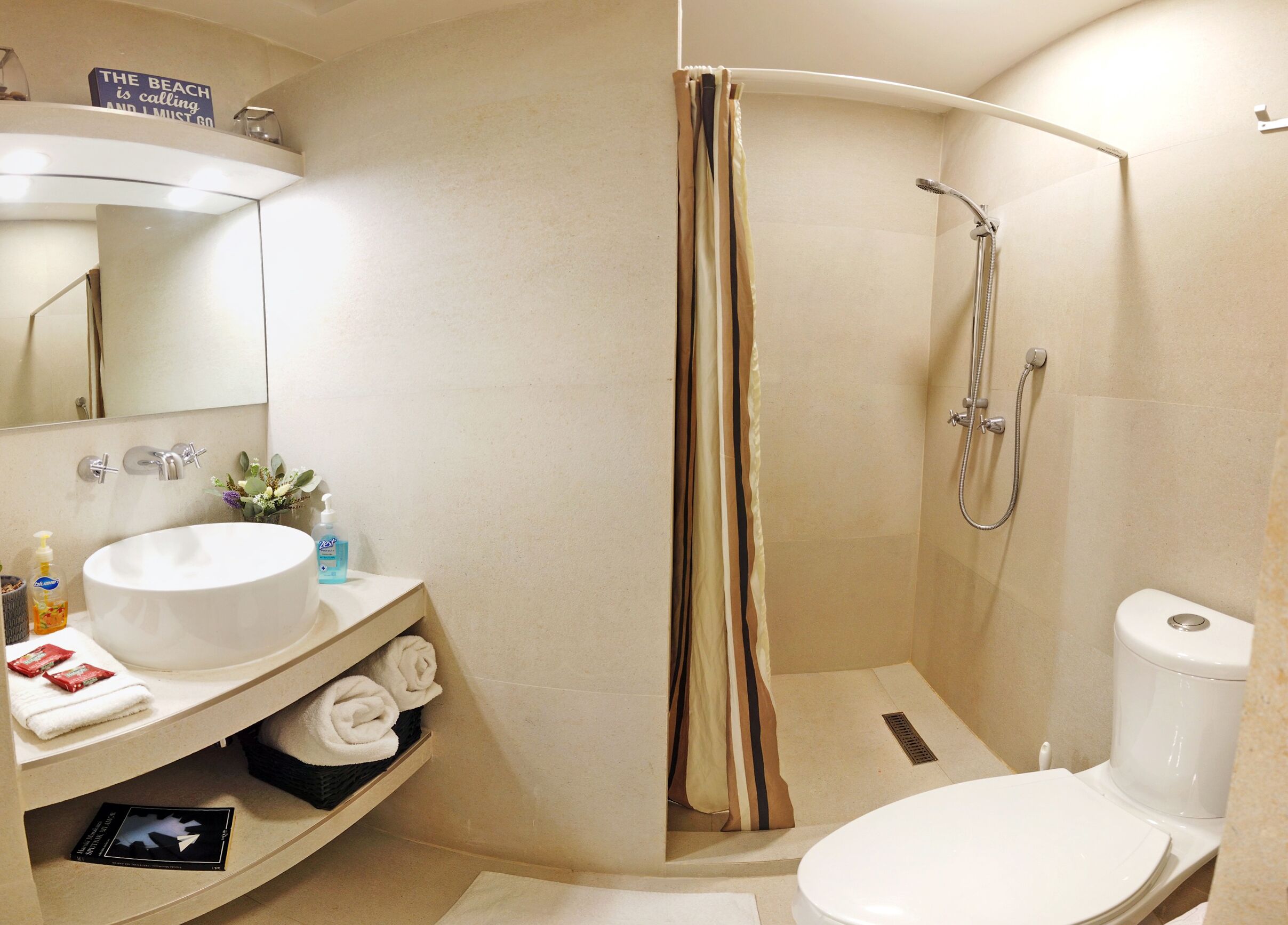 Une salle de bain avec un lavabo blanc, des toilettes et une douche avec un rideau de couleur beige.