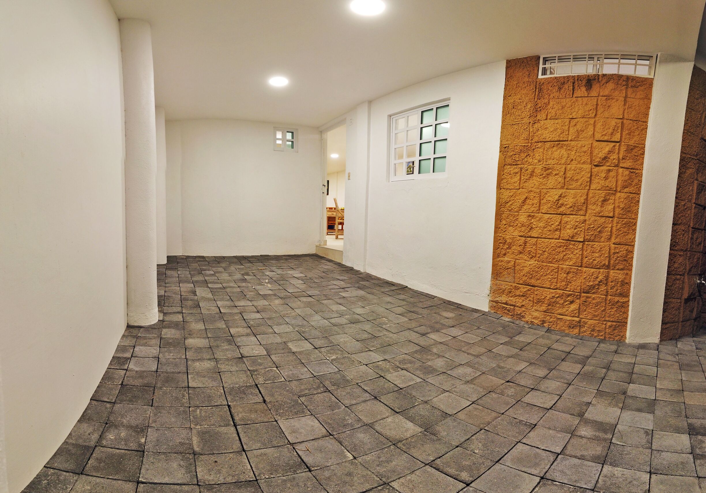 Ein Korridor mit Fliesenboden, weißen Wänden, einer Wand in Holzoptik und einem Fenster mit Gittermuster.