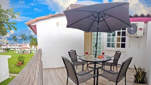 Une terrasse avec une table ronde, quatre chaises, un grand parasol et une plante en pot.