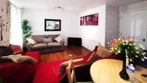 A living room with a sofa, a red couch, a wooden coffee table, and a floral arrangement. - London - 2 Bed Flat - Sleeps 4 - Parking - Wifi (London)