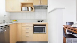 A compact kitchen with wooden cabinets, a stainless steel sink, a microwave, and a stove. - Darwin Esplanade Central (Darwin)