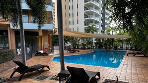 A swimming pool with lounge chairs and a tiled deck, surrounded by palm trees and a multi-story building. - Darwin Esplanade Central (Darwin)