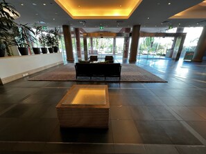 A spacious lobby with a central seating area, large windows, and potted plants.