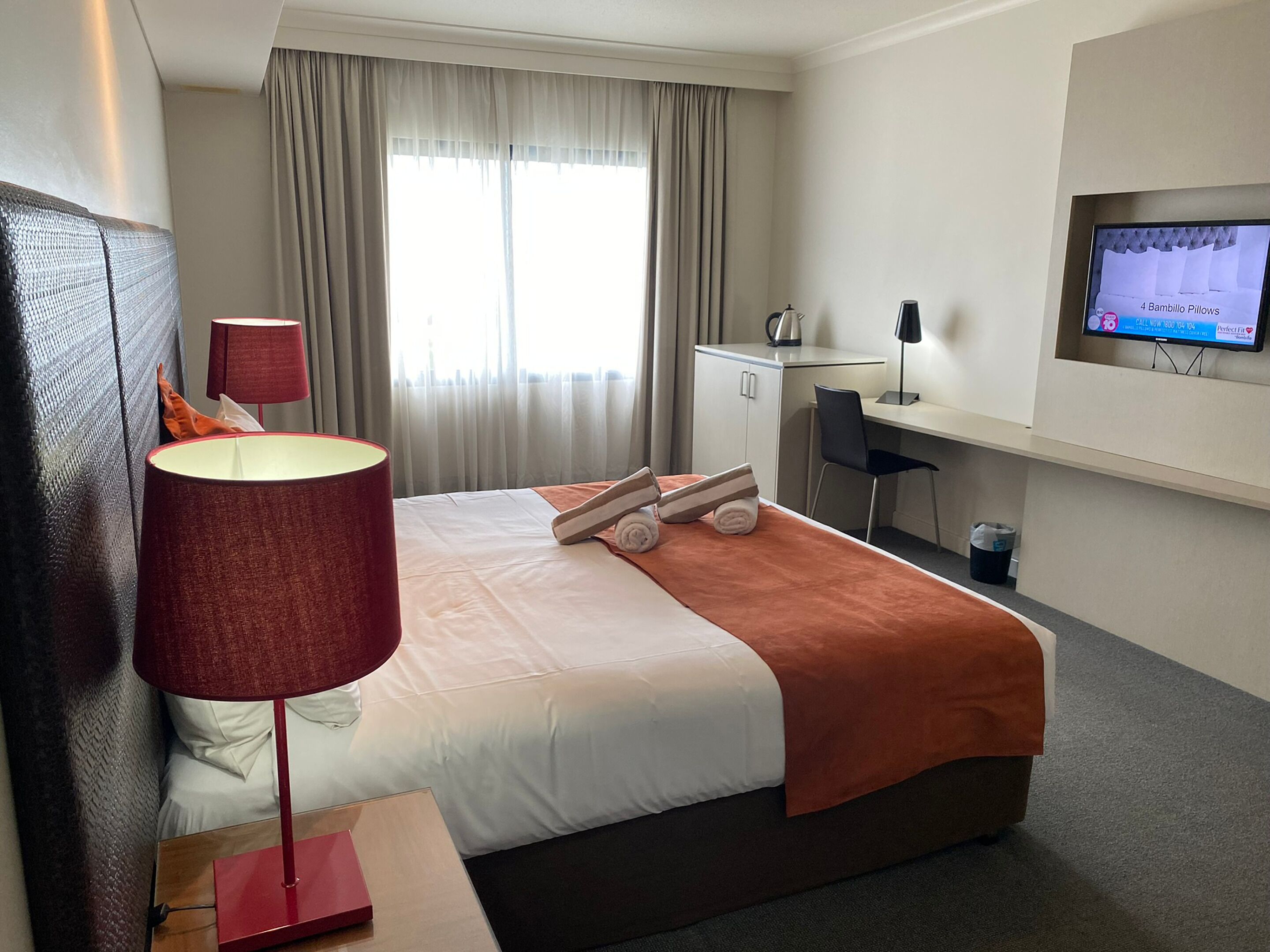 A hotel room with a bed, a desk, a chair, a TV, and a window with curtains.