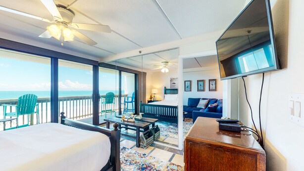 Una habitación de hotel con balcón, cama, escritorio, televisor y sofá.