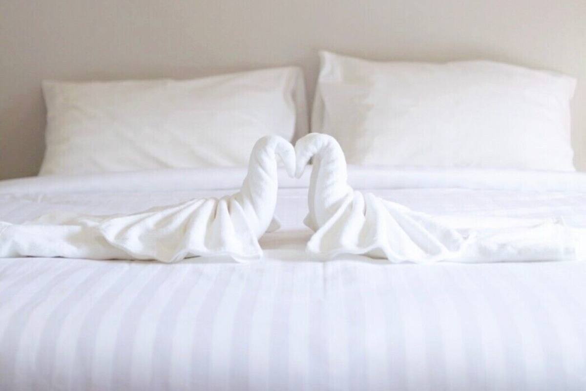 A hotel room with a bed, white pillows, and three framed artworks on the wall.