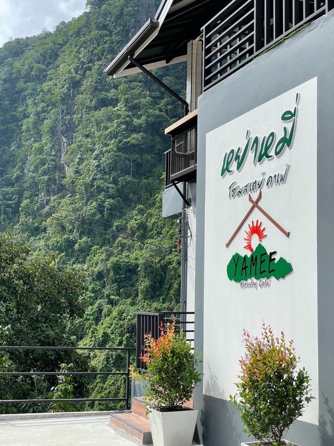 Un bâtiment orné d’une enseigne sur laquelle figure un logo et du texte, entouré d’une végétation luxuriante et avec une chaîne de montagnes en arrière-plan.