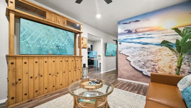 A living room with a large TV displaying 'Waikiki Promise Mountain' and a beach mural.