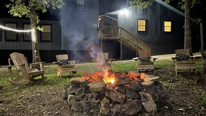 A fire pit with chairs around it, a wooden deck, and a building with a staircase in the background.