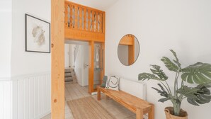 Un pasillo con un banco de madera, una planta en maceta, un espejo y un cuadro colgado en la pared.