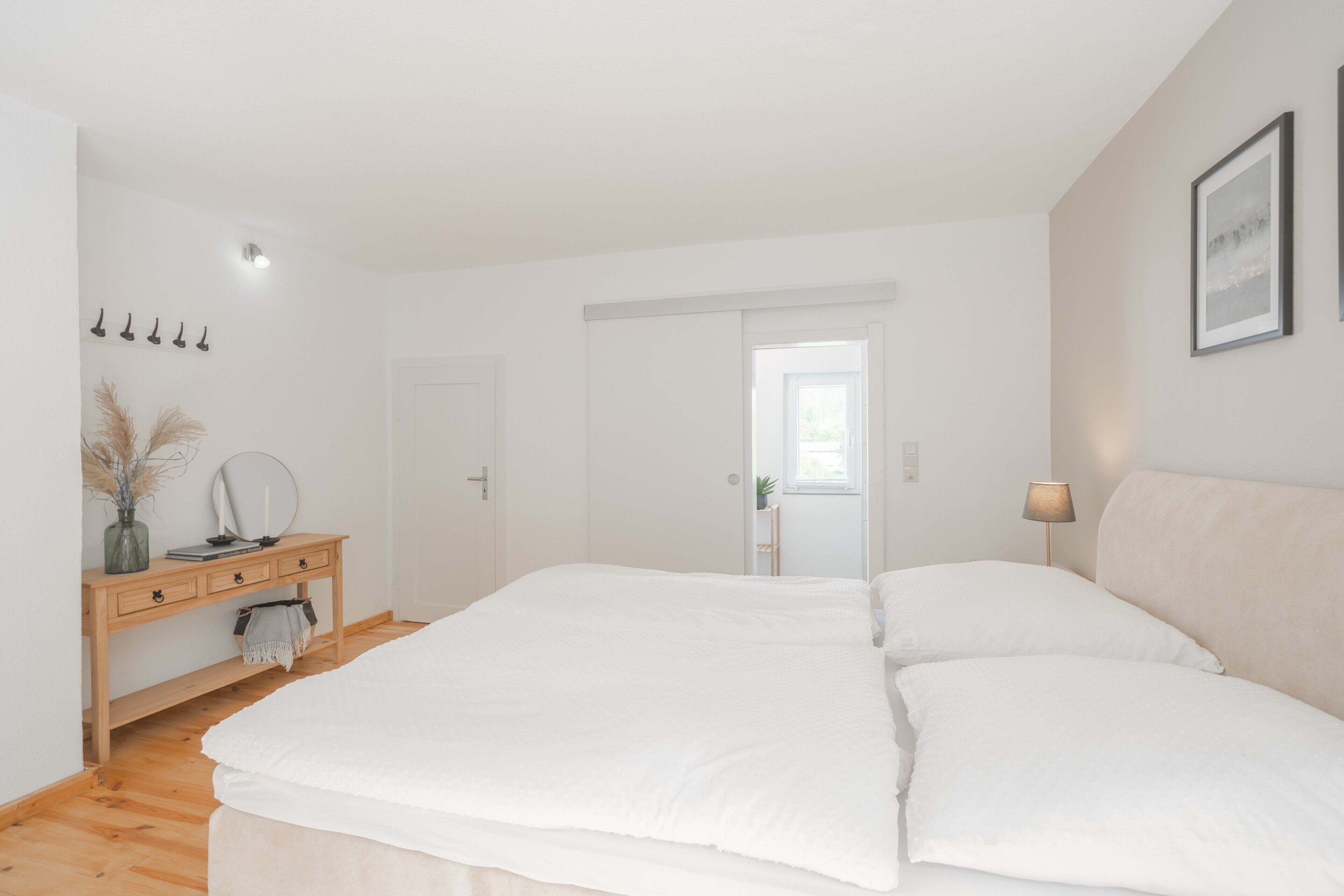 A bedroom with a large bed, a wooden dresser, a mirror, and a lamp.