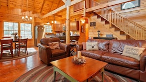 A cozy cabin interior with a wooden interior, a dining area, a living room with leather sofas, and a staircase. - Family Cabin on 20 Private Acres • Game Room • Near Berkeley Springs (Hancock)