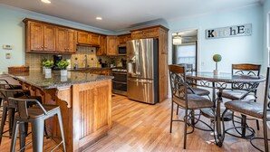 A modern kitchen with wooden cabinets, stainless steel appliances, and a bar area with stools. - 4BR Cozy Home, Close to UGA & Downtown Athens (Athens)