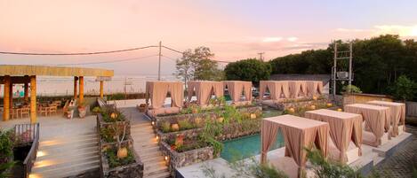 A rooftop pool area with covered seating and a view of the ocean.
