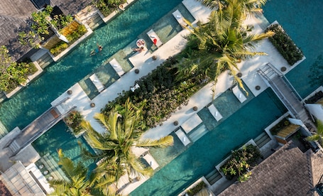 An aerial view of a resort with multiple swimming pools, sun loungers, and palm trees.
