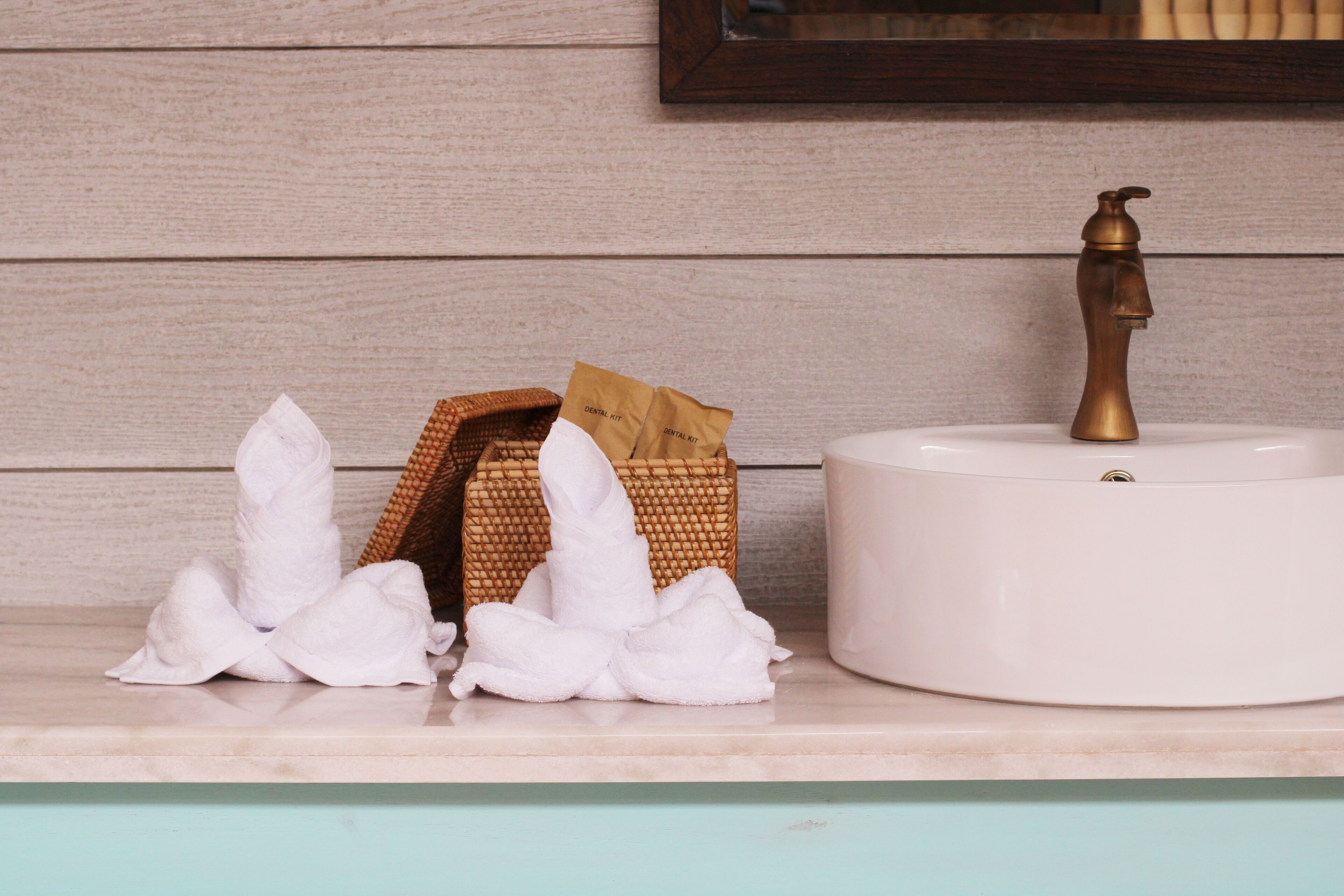 A bathroom sink with a brass faucet, a wicker basket with a white towel, and a white tissue box.
