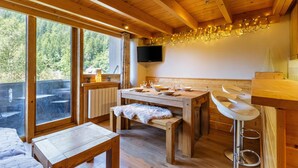 Un intérieur en bois comprenant une table à manger, un banc, un tabouret de bar et un téléviseur fixé au mur.