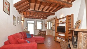 A living room with a red sofa, wooden ceiling beams, a fireplace, and a television. - Casa Guna, Asciano, Italy (Asciano)