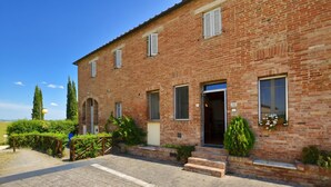 A brick building with a paved entrance, a small porch, and a window with a flower box. - Casa Guna, Asciano, Italy (Asciano)