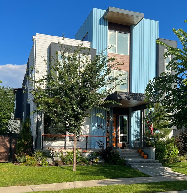 A modern two-story house with a blue and white exterior, a front porch, and a well-maintained garden.