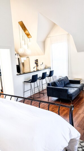 Cozy living space with a kitchenette, sofa, and bed, featuring a sloped ceiling and large window.