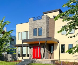 A modern two-story building with a red door, large windows, and a stone facade.