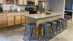 Una cocina moderna con armarios de madera, encimeras de granito y electrodomésticos de acero inoxidable, además de taburetes de bar.