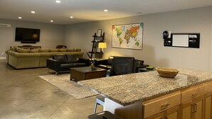Una sala de estar moderna con un televisor de pantalla plana grande, un sofá, una mesa de centro y una zona de cocina con encimeras de granito.