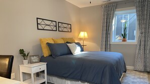 Un dormitorio con cama, mesita de noche, lámpara y ventana con cortinas.