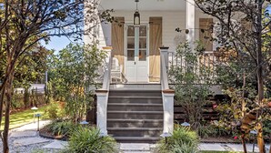 Uma casa com varanda, degraus que levam à porta e um jardim com diversas plantas e um caminho.