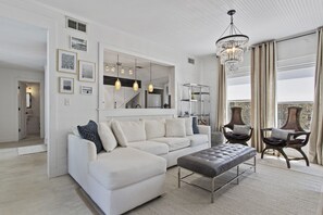 Una sala moderna con un sofá modular, un reposapiés capitonado y una araña.