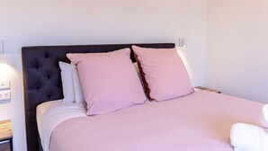 Una cama bien hecha con un cabecero oscuro y ropa de cama rosa.