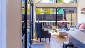 Un interior moderno con sofá, sillas y zona de comedor, que cuenta con ventanas amplias y suelo de madera.