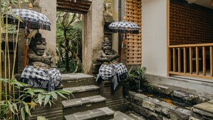 A stone statue with a checkered cloth, a checkered umbrella, and a wooden fence. - Wana Karsa Ubud Hotel (Ubud)