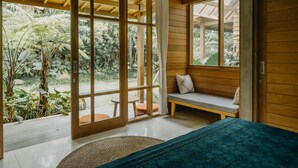 A room with a bed, a bench, and a view of a garden through large windows. - Wana Karsa Ubud Hotel (Ubud)