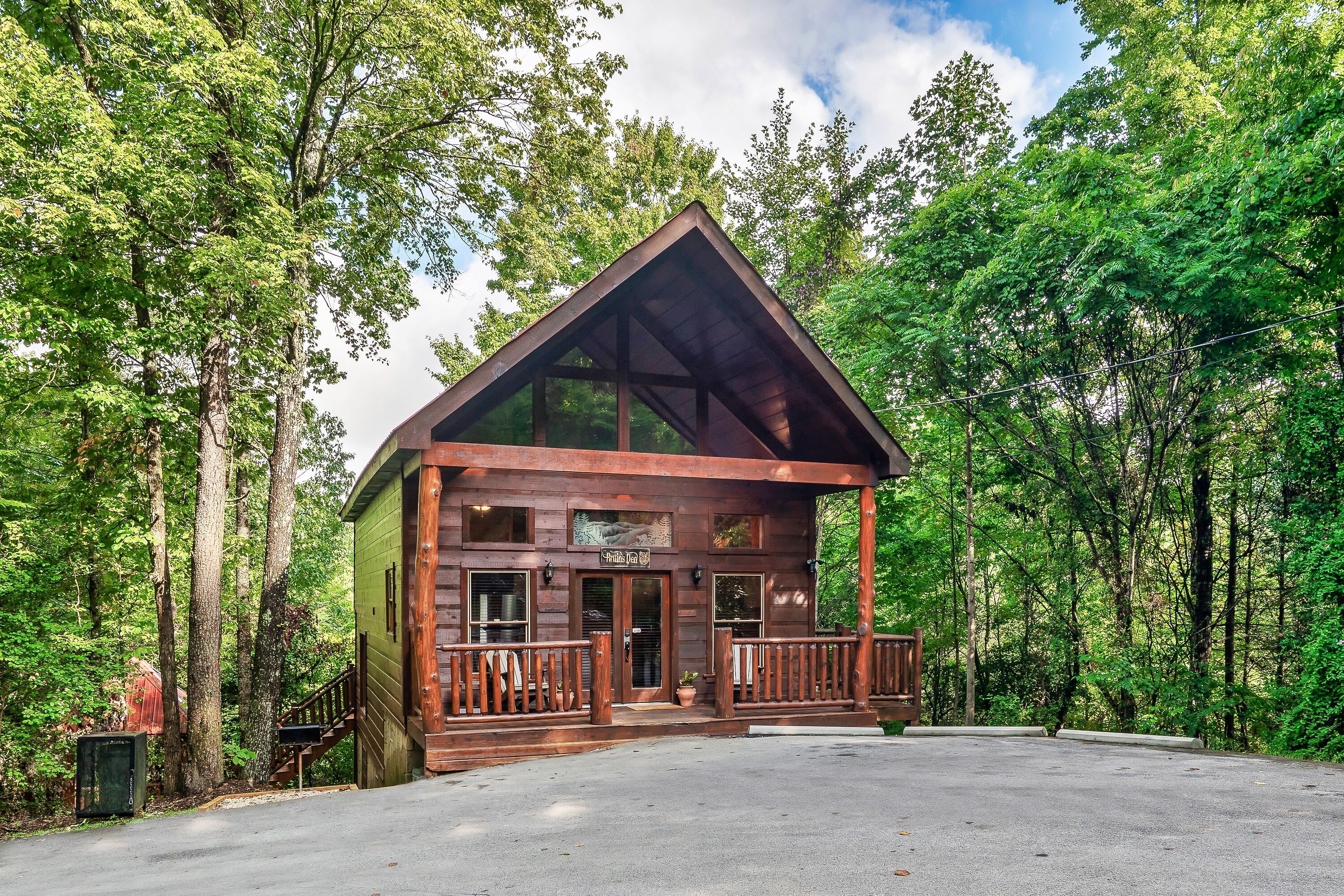 A wooden cabin with a glass front, surrounded by trees.