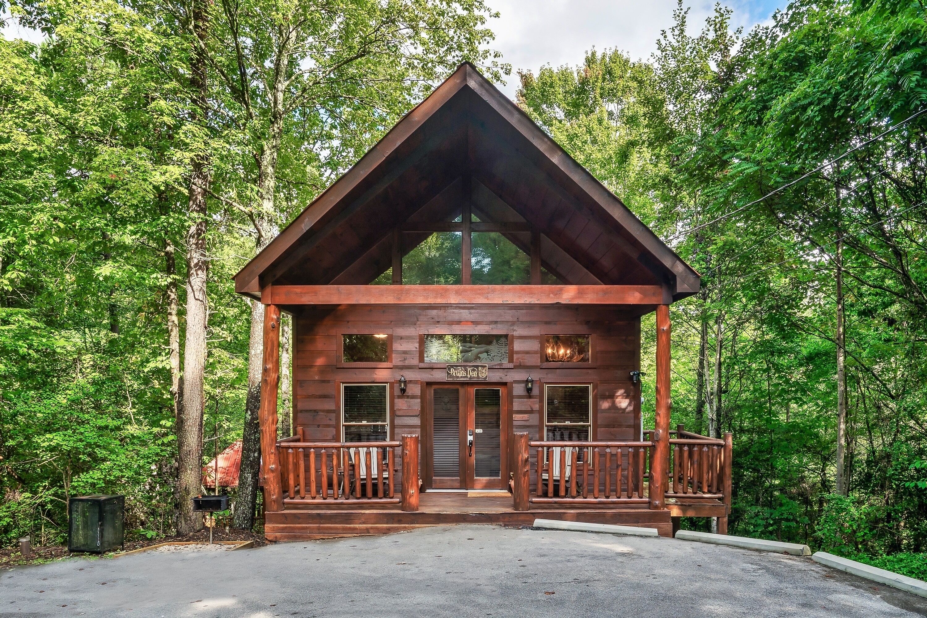 A wooden cabin with a porch, surrounded by trees.
