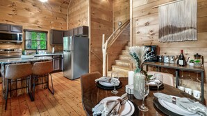Interior de una cabaña de madera con cocina, comedor y escalera.