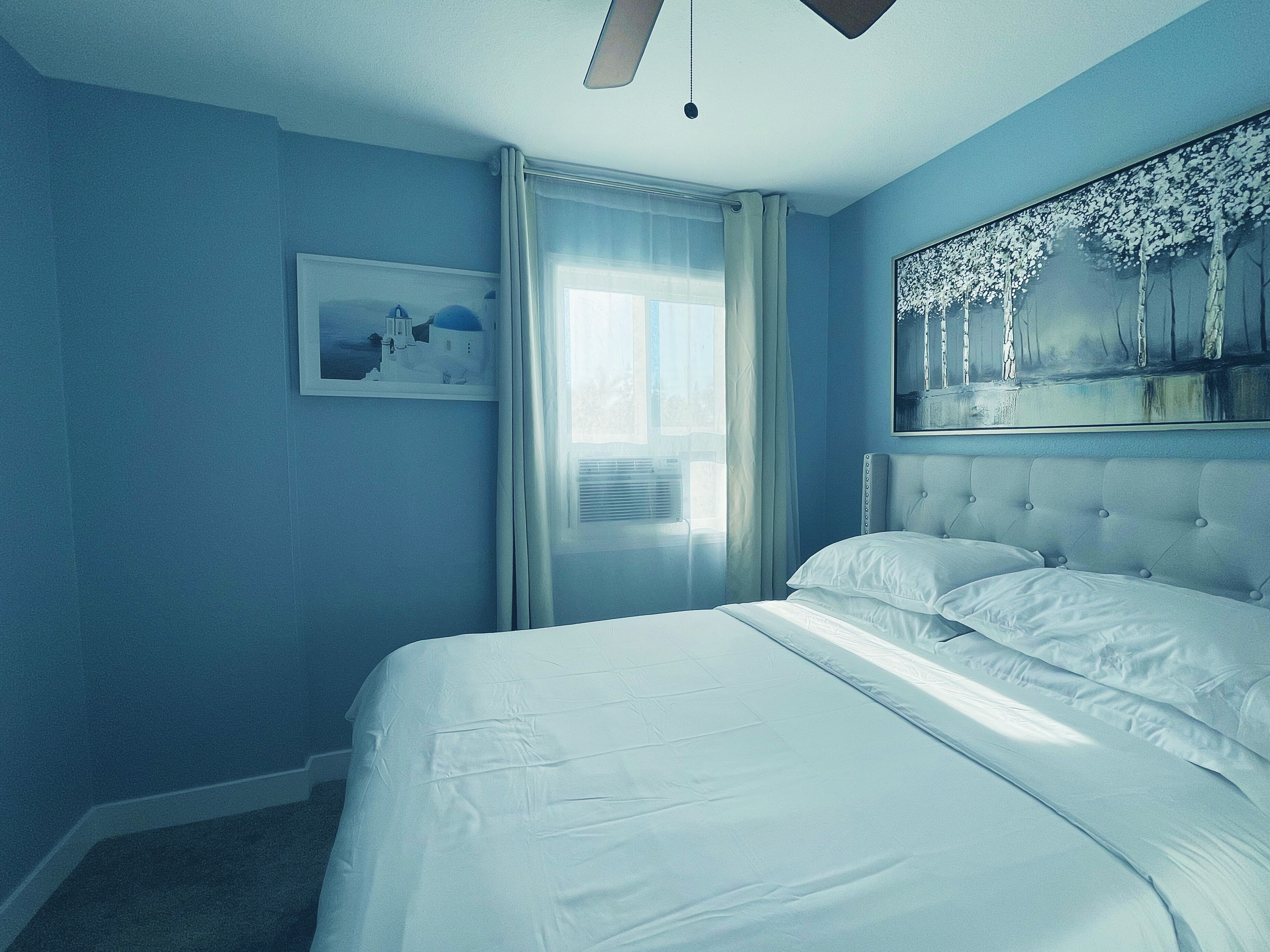 A bedroom with a large bed, a window with curtains, and a painting on the wall.