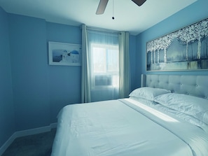 A bedroom with a large bed, a window with curtains, and a painting on the wall.
