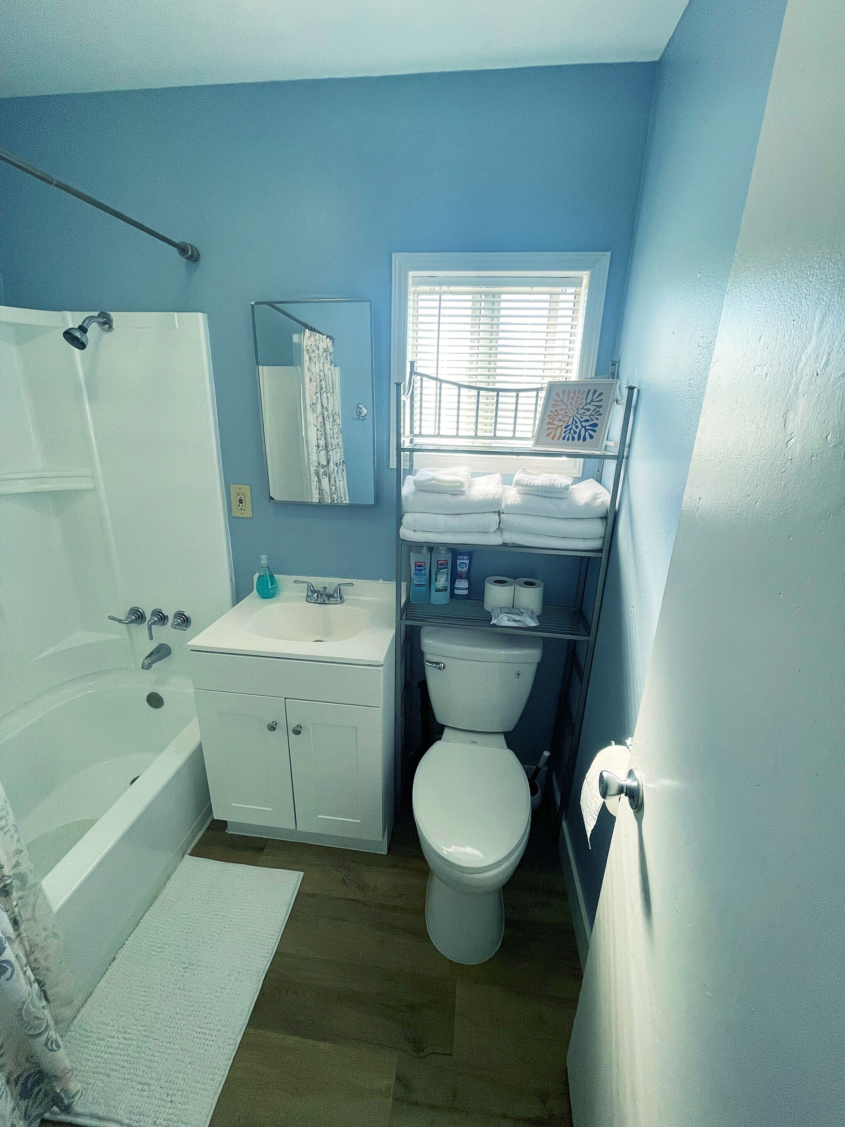 Ein Badezimmer mit Badewanne, Waschbecken, Toilette und einem Fenster mit Jalousien.