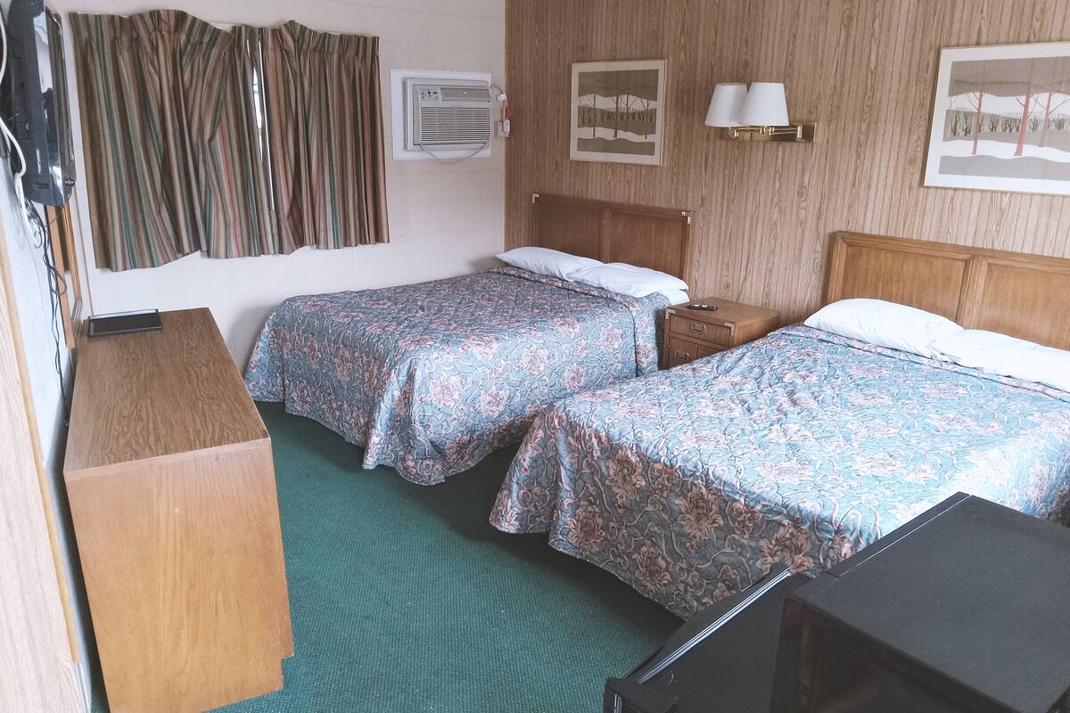 Une chambre d’hôtel avec deux lits, une tête de lit en bois, une table de chevet, un bureau et un téléviseur.