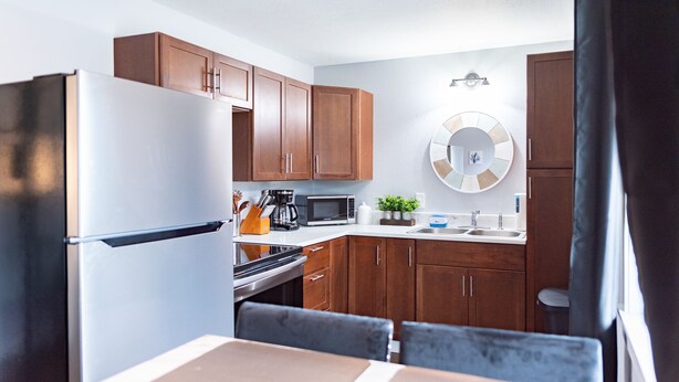 Una cocina compacta con armarios de madera, un refrigerador de acero inoxidable, un microondas y un lavamanos.