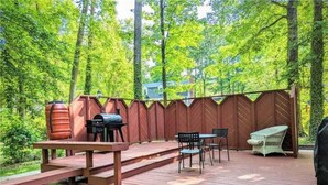 Una terraza de madera con una parrilla, mobiliario exterior y una zona cubierta.