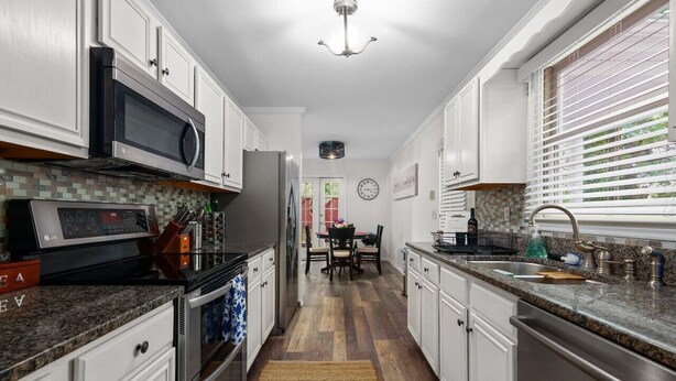 Una cocina con gabinetes blancos, microondas, refrigerador y pileta.