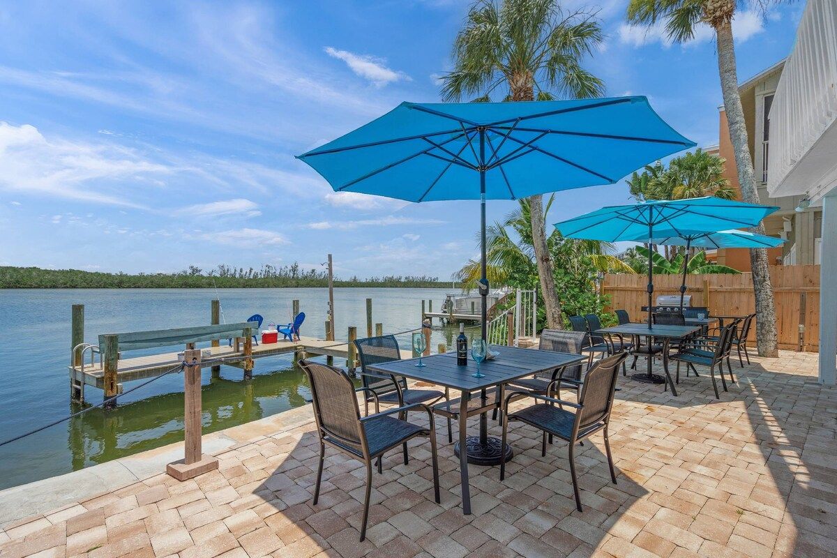 An outdoor patio with a table and chairs, a grill, and a view of the water.
