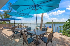 An outdoor patio with tables and chairs, umbrellas, and a view of a lake. - Siesta Key Base | Walk to Beach | Free Activities (Sarasota)